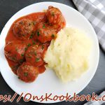 Wit bord met smeuïge aardappelpuree en balletjes in tomatensaus, gegarneerd met peterselie.