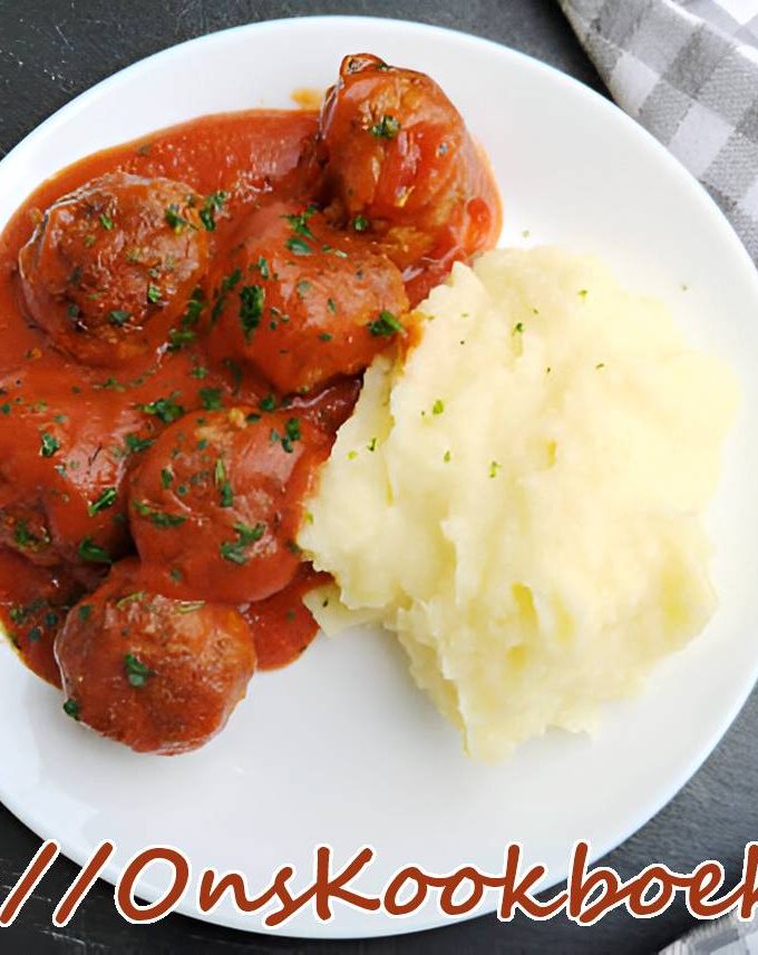 Wit bord met smeuïge aardappelpuree en balletjes in tomatensaus, gegarneerd met peterselie.