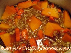 Pompoen, wortel en ui koken in bouillon voor romige pompoensoep volgens grootmoeders recept.