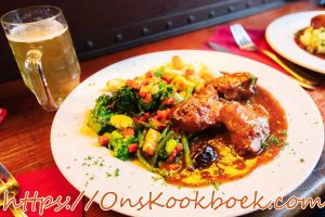 Konijn met pruimen en bier in Vlaamse saus, geserveerd met groenten en saus
