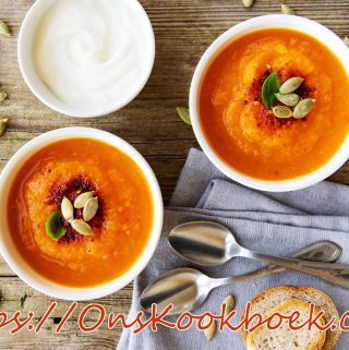 Romige pompoensoep met zoete aardappel en pompoenpitten, geserveerd met brood en crème fraîche