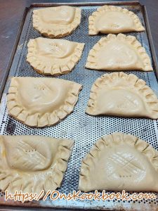 Ongebakken appelflappen met dichtgeknepen randen en gaatjes geprikt met vork: op geperforeerde bakplaat